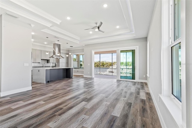 unfurnished living room featuring light wood-style floors, ornamental molding, and a raised ceiling