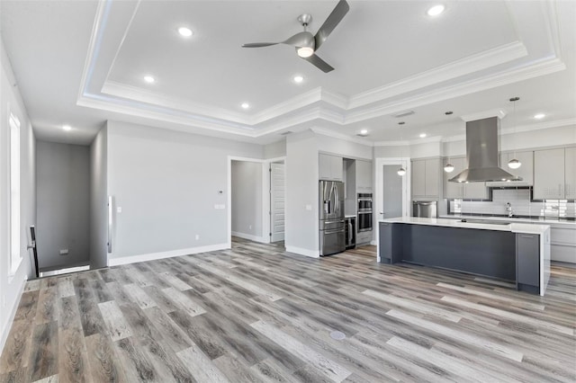 kitchen with a raised ceiling, stainless steel fridge with ice dispenser, island exhaust hood, light countertops, and gray cabinetry