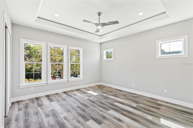 empty room featuring a tray ceiling, baseboards, and wood finished floors