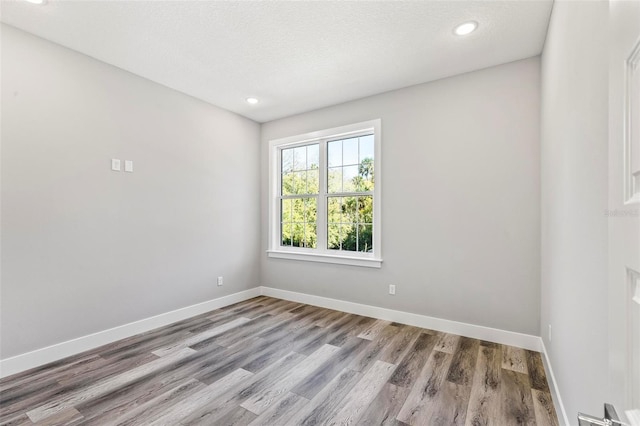 empty room featuring a textured ceiling, recessed lighting, wood finished floors, and baseboards