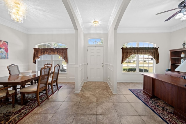 entrance foyer with light tile patterned floors, a decorative wall, a wainscoted wall, ceiling fan with notable chandelier, and crown molding