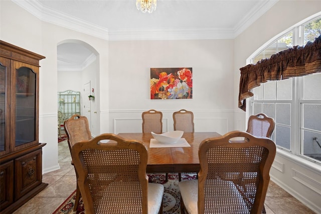 dining room with arched walkways, light tile patterned floors, a decorative wall, a wainscoted wall, and crown molding