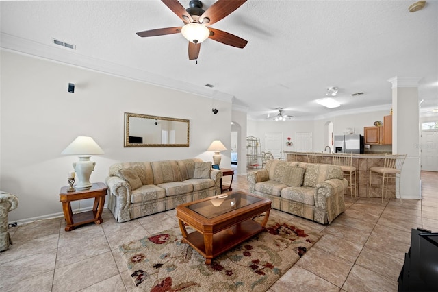 living area with visible vents, arched walkways, a ceiling fan, ornamental molding, and a textured ceiling