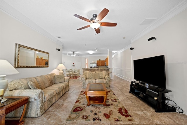 living room with light tile patterned floors, a ceiling fan, a decorative wall, and crown molding