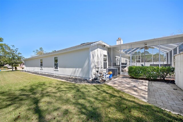 rear view of property with a chimney, a lawn, glass enclosure, a patio area, and central AC