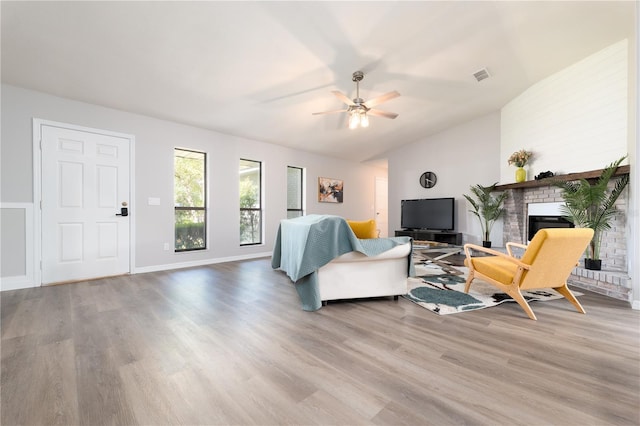 living area with visible vents, ceiling fan, wood finished floors, vaulted ceiling, and a brick fireplace