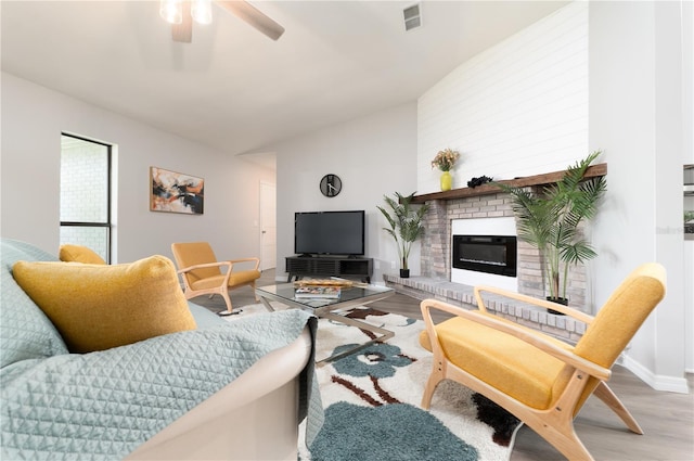 living room featuring a fireplace, visible vents, a ceiling fan, vaulted ceiling, and wood finished floors