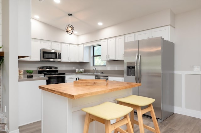 kitchen with a breakfast bar area, stainless steel appliances, wooden counters, white cabinets, and a sink