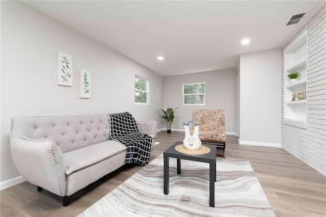 living area with built in shelves, wood finished floors, visible vents, and baseboards