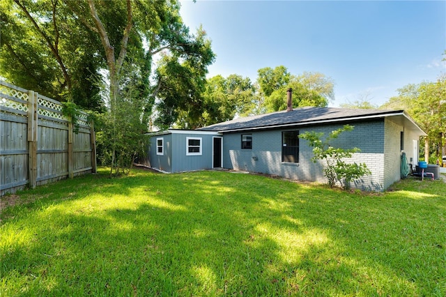 back of house featuring an outbuilding, brick siding, a yard, and fence