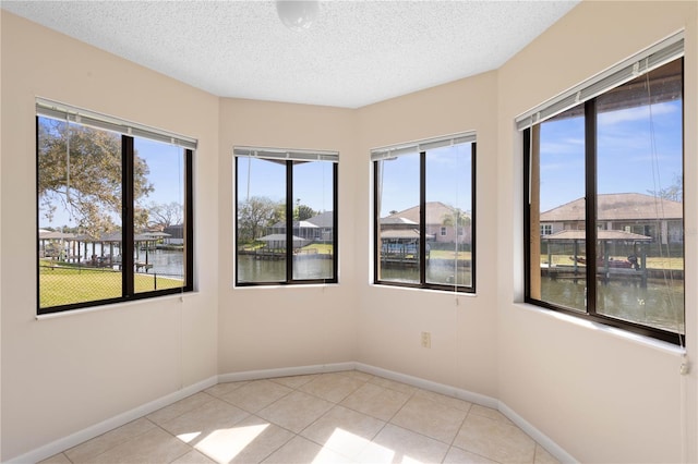 empty room featuring a textured ceiling, light tile patterned flooring, and baseboards