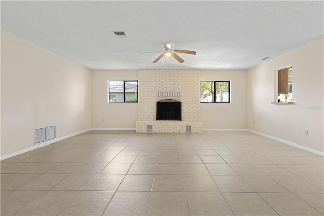 unfurnished living room with a brick fireplace, visible vents, a textured ceiling, and light tile patterned floors