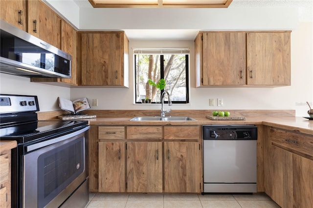 kitchen featuring light tile patterned floors, appliances with stainless steel finishes, brown cabinetry, and a sink