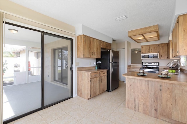 kitchen with light tile patterned floors, a textured ceiling, a sink, light countertops, and appliances with stainless steel finishes