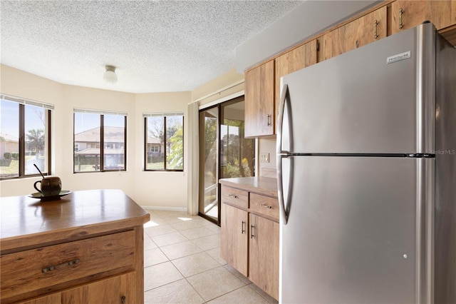 kitchen with light tile patterned floors, plenty of natural light, a textured ceiling, and freestanding refrigerator