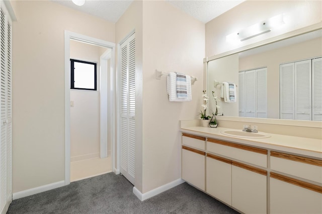 bathroom with a textured ceiling, vanity, baseboards, a closet, and carpet