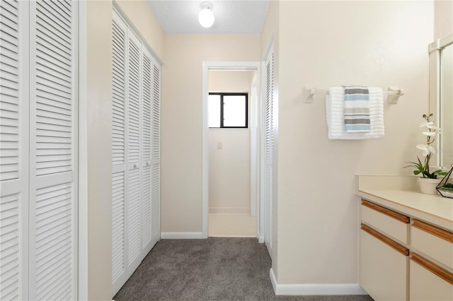 hall with a textured ceiling, carpet, and baseboards