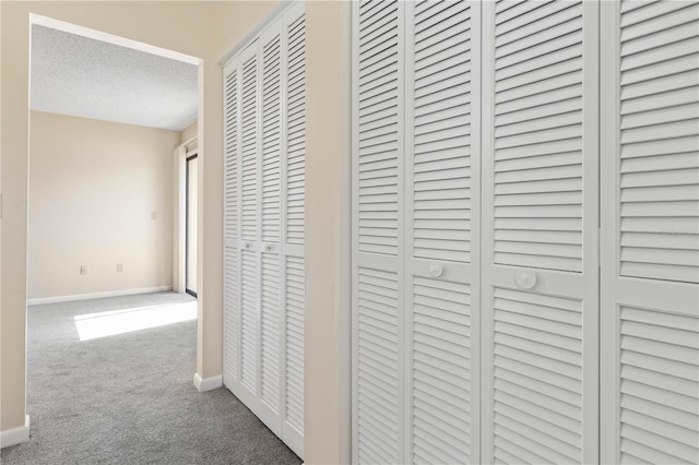 hallway with a textured ceiling, carpet, and baseboards