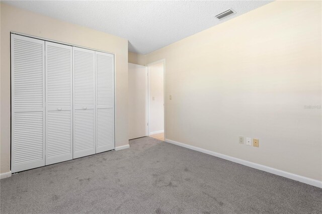 unfurnished bedroom with baseboards, visible vents, carpet, a textured ceiling, and a closet