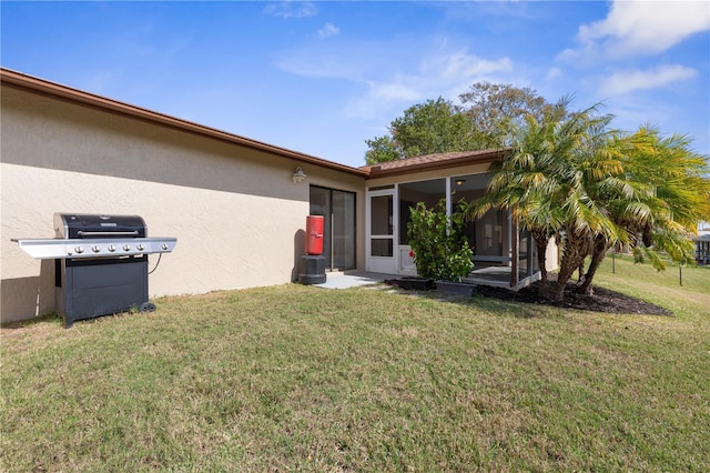 rear view of house with a sunroom, a yard, and stucco siding