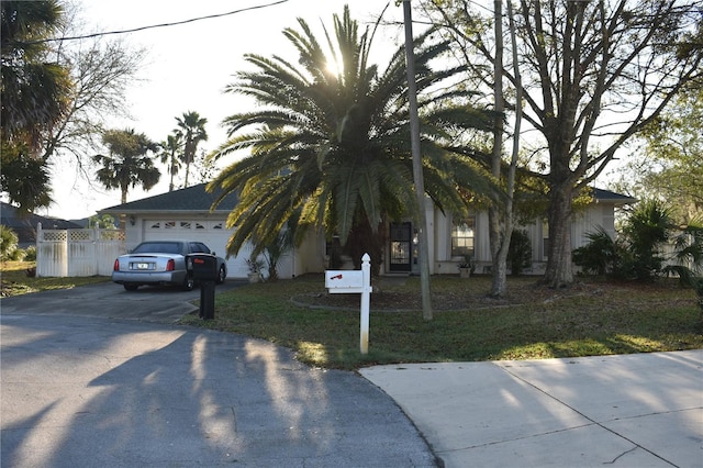 view of property hidden behind natural elements featuring driveway, an attached garage, and fence