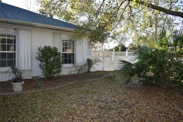 view of side of home with a shingled roof, fence, and stucco siding