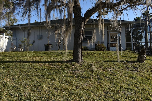 view of property exterior with a lawn, stucco siding, fence, and a lanai