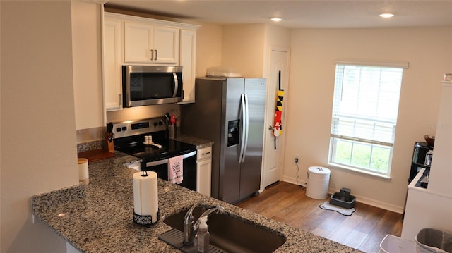 kitchen with appliances with stainless steel finishes, stone countertops, white cabinetry, a sink, and wood finished floors