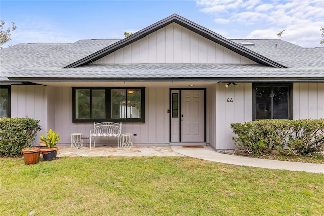 view of front of house with a shingled roof, a front lawn, and board and batten siding