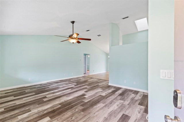 spare room featuring visible vents, lofted ceiling with skylight, a ceiling fan, wood finished floors, and baseboards