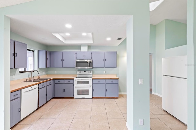 kitchen featuring a tray ceiling, gray cabinets, visible vents, a sink, and white appliances