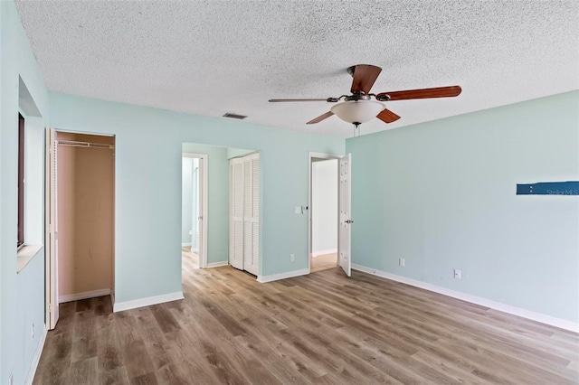 unfurnished bedroom featuring baseboards, a textured ceiling, visible vents, and wood finished floors