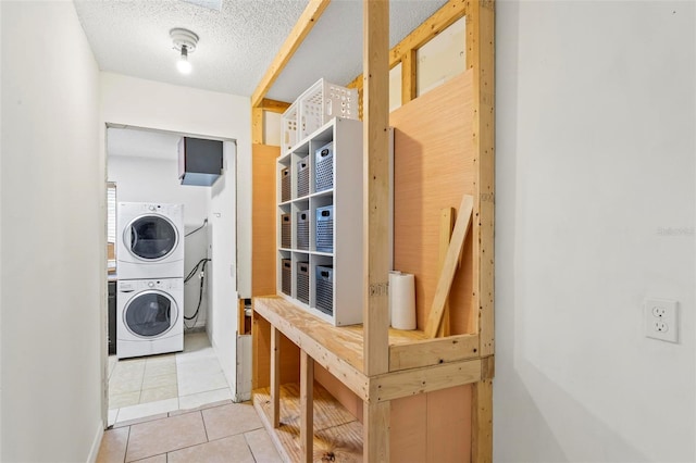 washroom featuring a textured ceiling, laundry area, stacked washing maching and dryer, and tile patterned floors