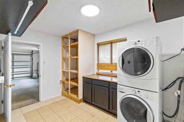 clothes washing area featuring a textured ceiling, light tile patterned flooring, stacked washing maching and dryer, and cabinet space