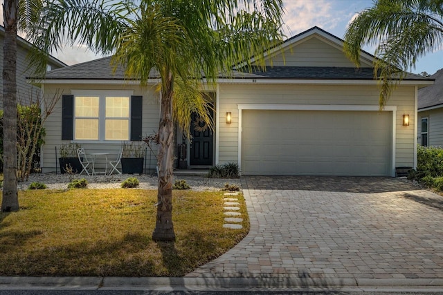 ranch-style home featuring a garage, a front yard, decorative driveway, and roof with shingles