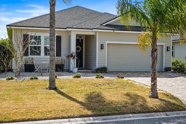 view of front of property featuring a garage, decorative driveway, a shingled roof, and a front lawn