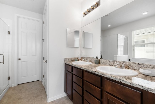 bathroom featuring double vanity, a stall shower, a sink, and baseboards