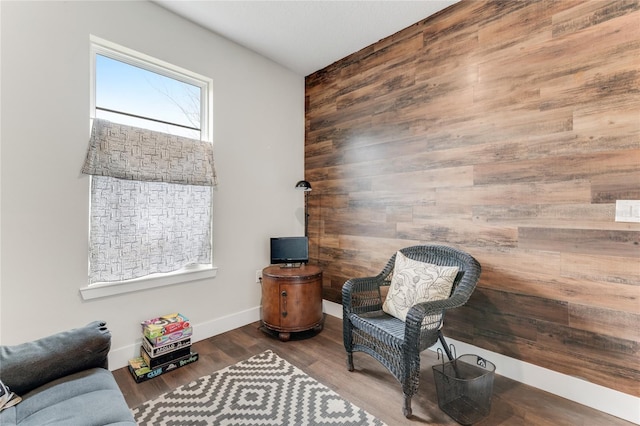 sitting room featuring an accent wall, wood walls, baseboards, and wood finished floors