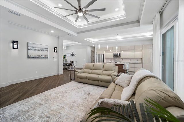 living area with visible vents, a ceiling fan, ornamental molding, dark wood-style flooring, and a tray ceiling