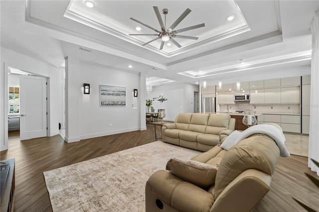 living room featuring wood finished floors, visible vents, a ceiling fan, ornamental molding, and a tray ceiling