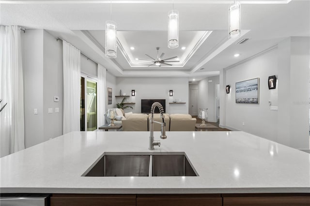 kitchen featuring a raised ceiling, open floor plan, a kitchen island with sink, light countertops, and a sink