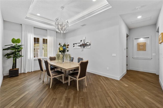 dining room with a tray ceiling, wood finished floors, visible vents, and baseboards