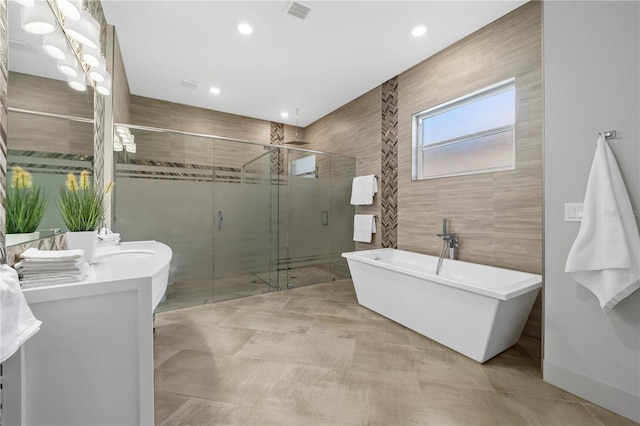 full bathroom featuring a stall shower, visible vents, a soaking tub, vanity, and tile walls