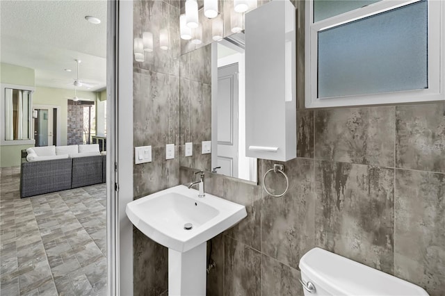 bathroom with toilet, ceiling fan, a textured ceiling, and tile walls