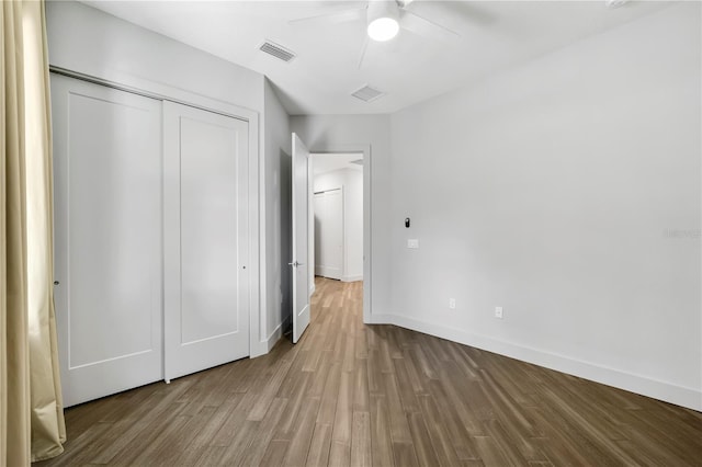 unfurnished bedroom with wood finished floors, a ceiling fan, visible vents, baseboards, and a closet