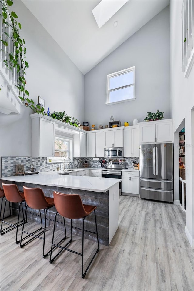 kitchen featuring a breakfast bar area, stainless steel appliances, white cabinets, high vaulted ceiling, and a peninsula