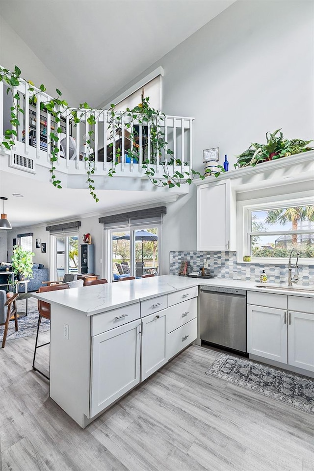 kitchen featuring decorative backsplash, a peninsula, stainless steel dishwasher, white cabinetry, and a sink