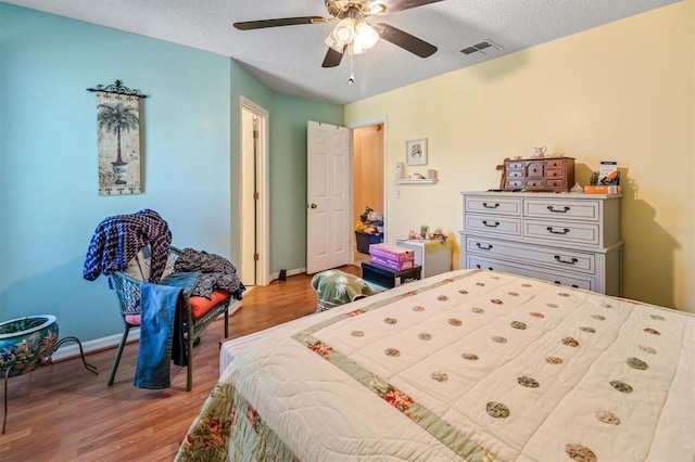 bedroom with a textured ceiling, wood finished floors, visible vents, and baseboards