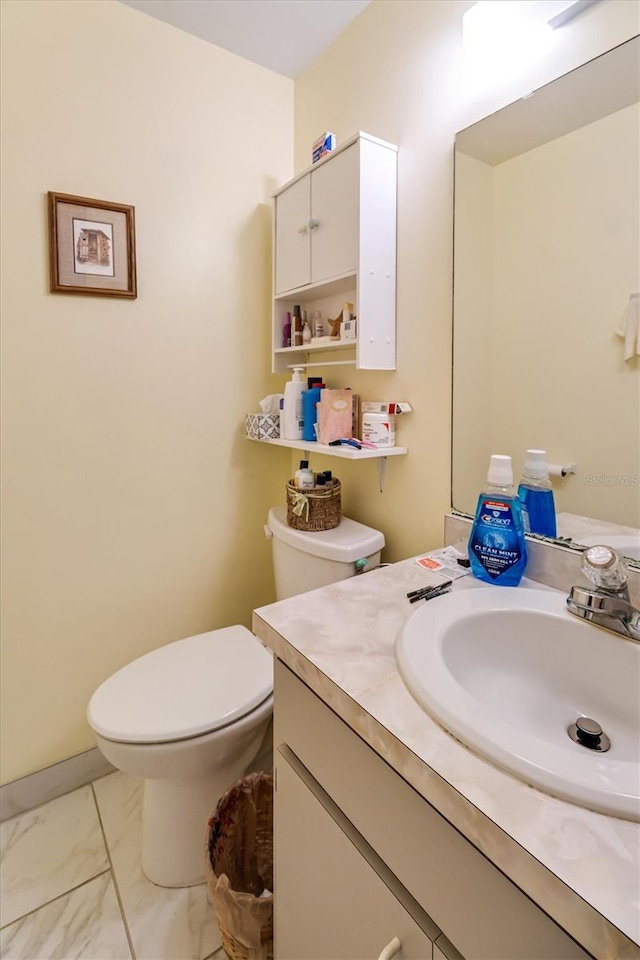 half bath with marble finish floor, vanity, and toilet