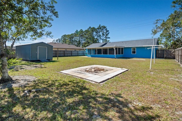 view of yard featuring an outdoor fire pit, a sunroom, a fenced backyard, an outbuilding, and a storage unit